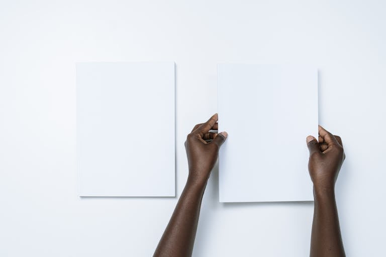 Top view of two hands holding blank white sheets against a minimalistic background.