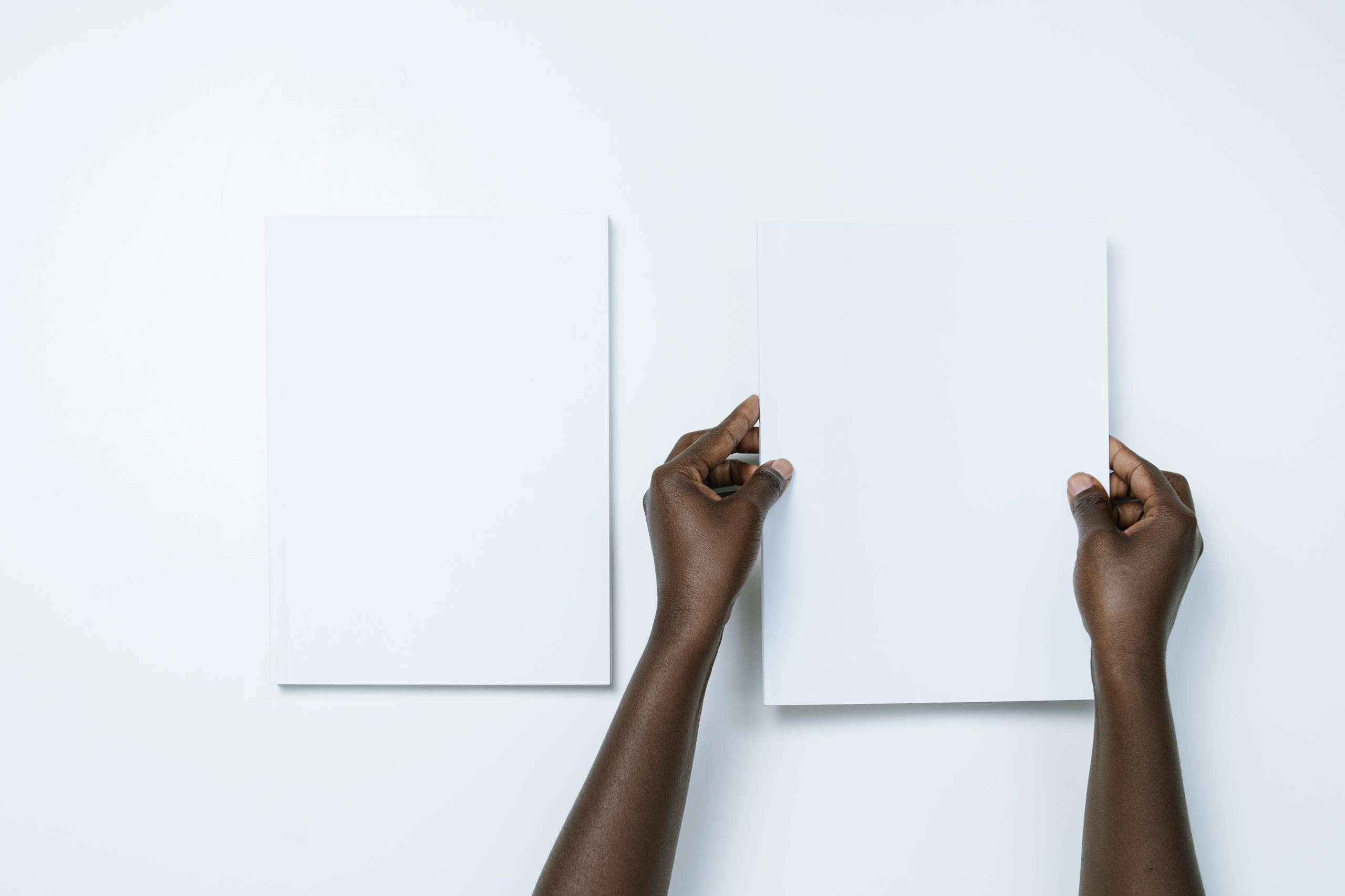 Top view of two hands holding blank white sheets against a minimalistic background.